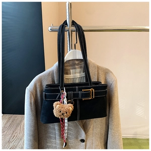 Detail of black underarm bag with contrast stitching and plush bear charm on a suit