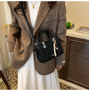 Detail einer schwarzen Mini-Tasche aus Leder mit Lychee-Struktur, Perlenanhänger und Gurt