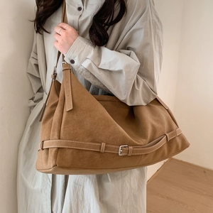 Detail of tan suede tote bag with adjustable buckle strap shown on model's shoulder