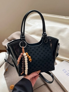 Sac seau noir chic à motif damier avec breloque en bois dans un décor urbain moderne