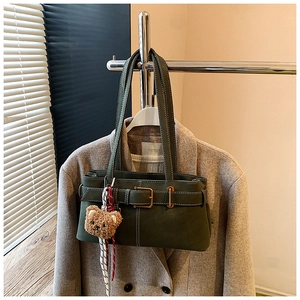 Detail of dark green underarm bag featuring contrast stitching and a cute plush bear charm