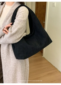 Sac cabas minimaliste en daim noir avec bandoulière large dans un décor intérieur