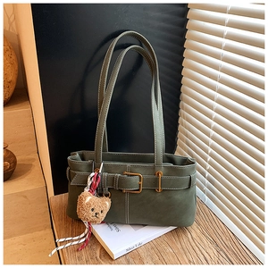Close-up of dark green rectangular shoulder bag with vintage metal buckle and plush bear charm