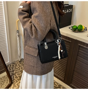 Schwarze Umhängetasche mit Litschi-Muster und Perlenanhänger über braunem Blazer
