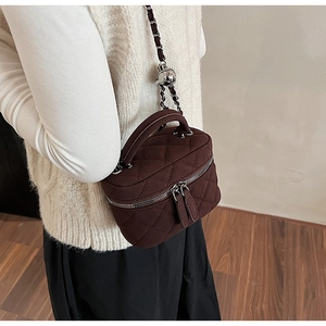 Close-up of quilted dark brown matte crossbody bag with chain strap worn by a model