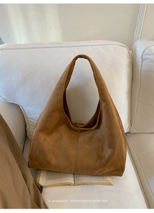 Détail de la texture d'un sac hobo en daim caramel sur un canapé blanc minimaliste