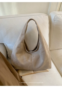 Détail de la texture d'un sac hobo en daim kaki posé sur un canapé en tissu minimaliste