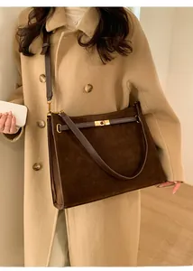 Détail d'un grand cabas en daim marron avec fermoir doré porté sur un manteau beige