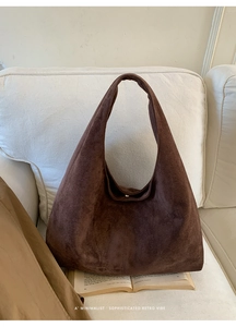 Détail du sac à bandoulière en daim marron foncé avec fermoir magnétique sur canapé