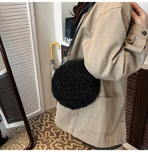 Close-up of black fleece circle crossbody bag with metal hooks and slim leather strap