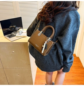 Detailaufnahme der braunen Leder-Handtasche mit gewebtem Griff und Perlen-Anhänger