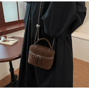 Detail of brown quilted suede bucket bag with gold chain strap and metal ball charm