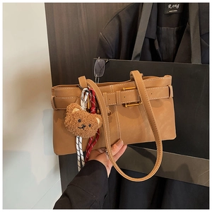 Detail of brown faux leather shoulder bag with white stitching and bear plush pendant