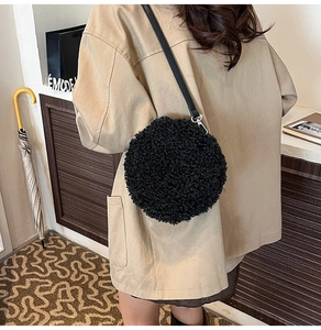 Detail of a black plush round crossbody bag with faux lamb wool texture on a model