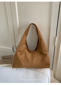 Détail d'un grand sac cabas en daim marron contre une porte en bois blanc minimaliste