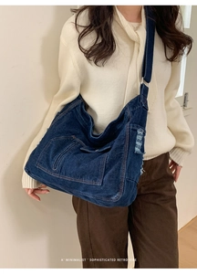 Detail of blue denim crossbody bag featuring distressed fabric and front zipper pocket