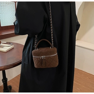Detail view of a brown quilted suede mini vanity bag with chain strap worn on the shoulder