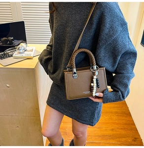 Detailaufnahme der braunen Ledertasche mit Flechtgriff und stilvollem Perlenanhänger