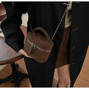 Detail of a brown quilted suede mini bag with silver chain strap and top handle design