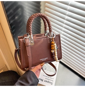 Detailaufnahme der dunkelbraunen Lederhandtasche mit gewebtem Griff und Perlenanhänger