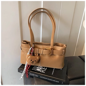 Detail shot of khaki shoulder bag with metal buckle and plush bear charm on books