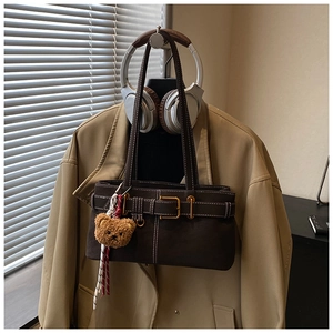 Detail of dark brown retro shoulder bag with golden buckle and cute bear charm pendant