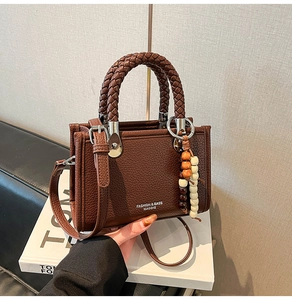 Detail der dunkelbraunen Litschi-Ledertasche mit gewebtem Griff und Perlen-Anhänger