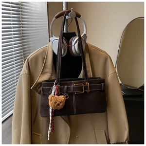 Detail of dark brown suede shoulder bag with contrast stitching and bear charm