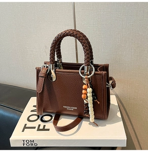Detail der braunen Lederhandtasche mit gewebtem Griff und buntem Perlen-Quasten-Anhänger