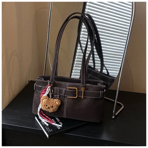 Detail of dark brown matte leather shoulder bag with bear pendant and white stitching