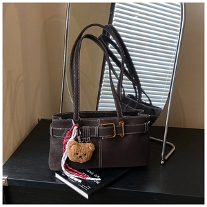 Detail of dark brown suede shoulder bag with contrast stitching and teddy bear charm