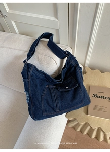 Detail of blue denim tote bag with frayed edges and wide strap on white sofa
