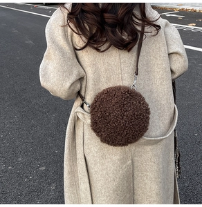 Detail of round faux shearling bag in brown with slim leather strap and metal hooks