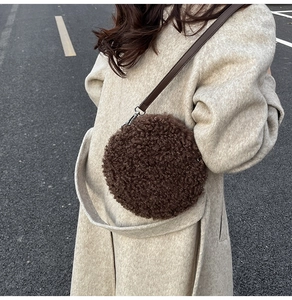 Detail of round plush crossbody bag in dark brown fleece with leather strap and metal hooks