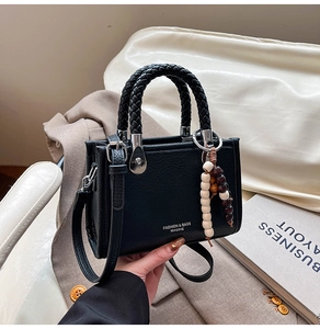 Detail einer schwarzen Handtasche mit Litschi-Muster, Webgriffen und Holzperlenanhänger