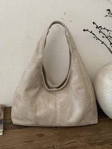 Sac fourre-tout minimaliste en daim beige avec large bandoulière sur table en bois rustique