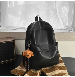 Detail of black faux leather backpack featuring a cute brown plush puppy charm on the zipper