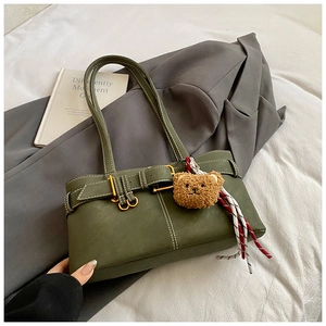 Olive green tote bag detail with decorative buckle, plush bear charm, and white stitching