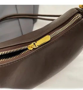 Close-up of smooth gold metal zipper on premium brown leather shoulder bag detail