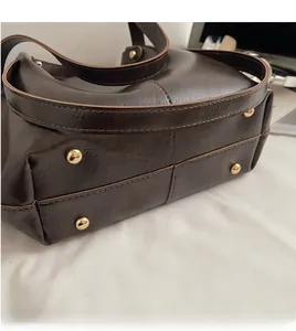 Détail du fond d'un grand sac cabas marron foncé avec quatre pieds de protection dorés