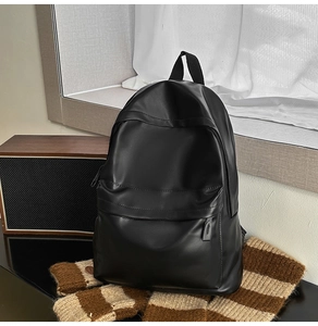 Close-up of a black matte PU leather backpack featuring a front zipper pocket detail