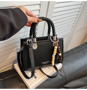 Detail der schwarzen Handtasche mit Litschi-Struktur, Webgriffen und Holzperlen-Deko