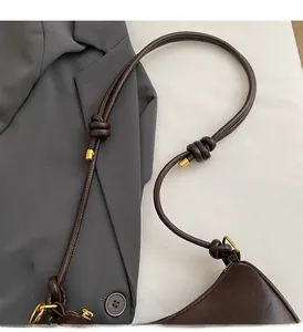 Detail of dark brown leather shoulder bag featuring knotted strap and gold hardware