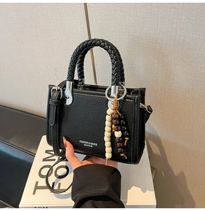 Detail der schwarzen Handtasche aus genarbtem Leder mit geflochtenem Griff und Perlen