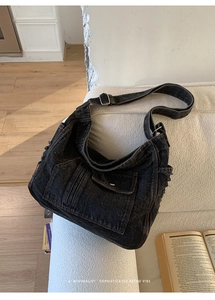 Detail view of washed black denim hobo bag with raw edge pocket on a white sofa
