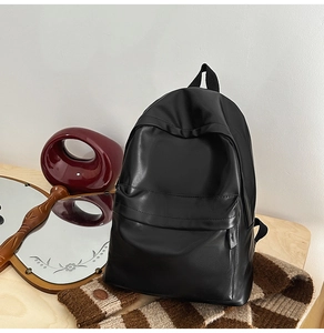 Detail of minimalist black faux leather backpack on a wooden table with decor
