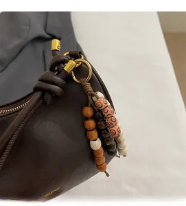 Close-up of brown leather handbag featuring colorful wooden bead tassel and gold hardware