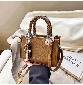 Detail der braunen Lederhandtasche mit gewebtem Griff und Perlenanhänger-Accessoire