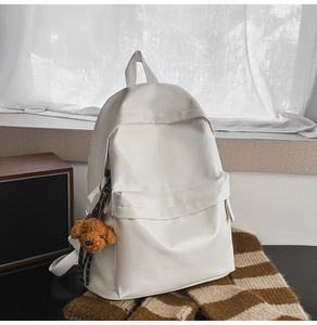 Close-up of cream minimalist backpack featuring a plush dog charm and zip pocket