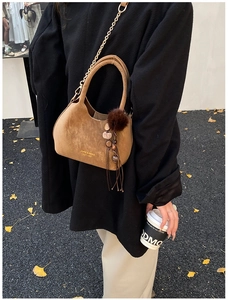 Gros plan du sac seau en daim marron avec chaîne dorée et breloque bohème à franges
